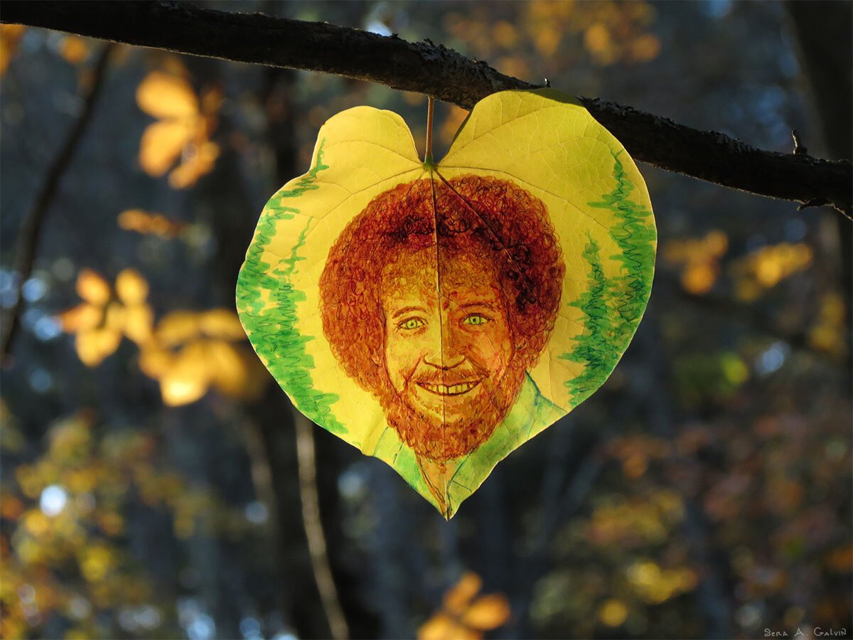 A smiling Bob Ross with green evergreens, drawn on a yellow heart-shaped leaf hanging from a branch, by Sera Autumn
