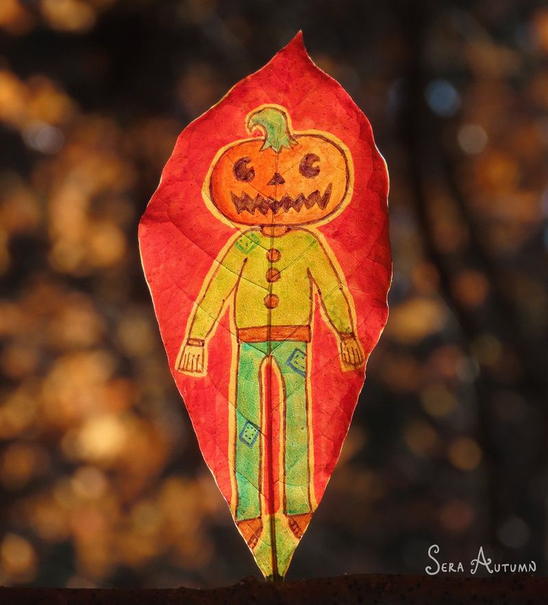 A jack-o'-lantern-headed scarecrow figure drawn on a red leaf, backlit against golden bokeh, by Sera Autumn