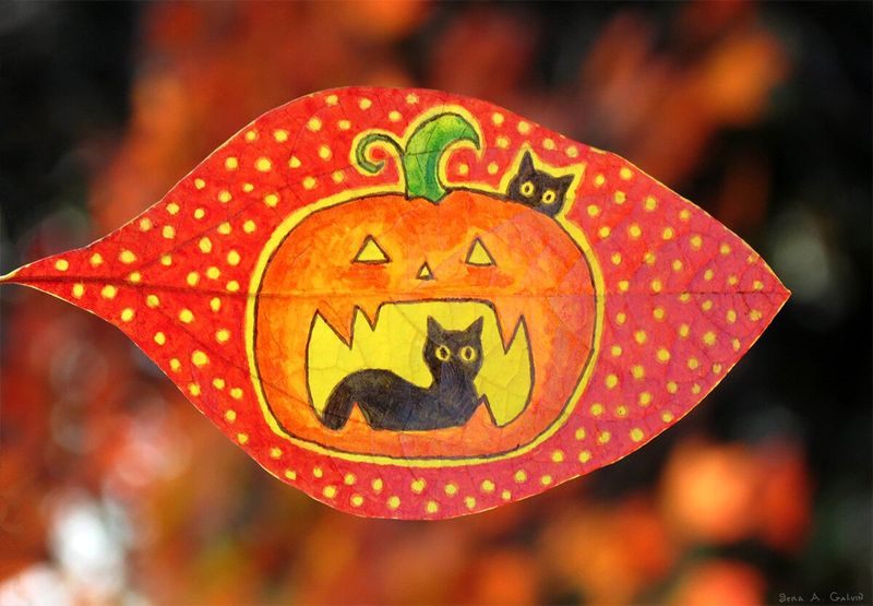 A grinning carved jack-o'-lantern holding one black cat inside its mouth and a kitten peeking over the top, on a red polka-dotted leaf against fiery bokeh, by Sera Autumn
