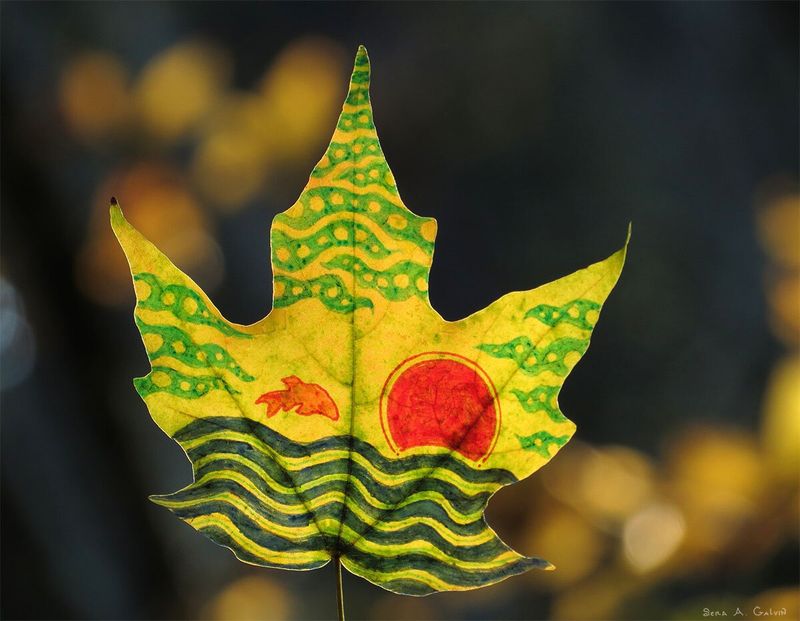 An orange fish leaping over dark rolling waves beneath a red setting sun, drawn on a patterned green-and-yellow maple leaf, by Sera Autumn